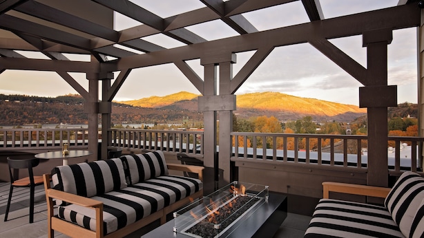 A covered outdoor seating area with a fire feature, wooden furniture, and a view of a hilly landscape. - Lightwell Hotel & Spa (Hood River)