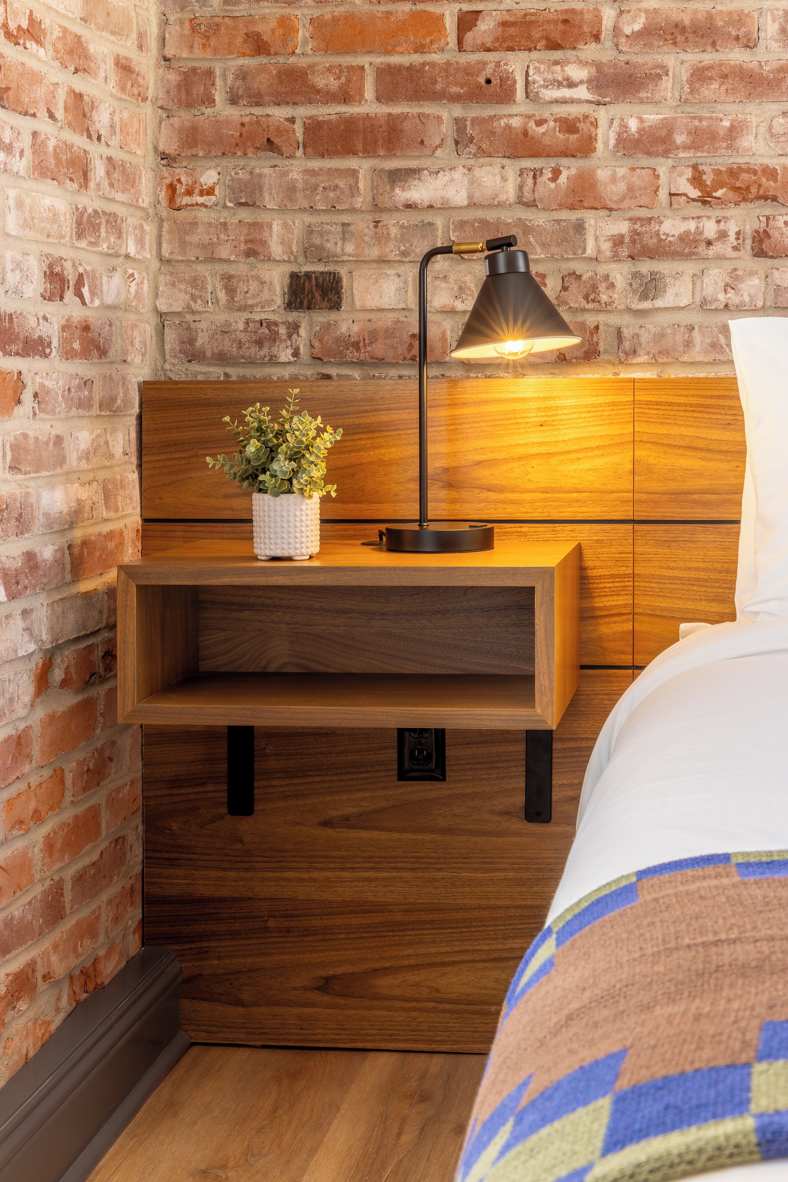 A wooden bedside table with a lamp, a small plant, and a drawer.