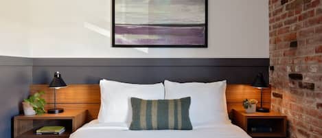 A hotel room with a bed, two nightstands, a wall-mounted painting, and a brick wall.