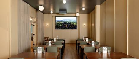 A conference room with wooden tables and chairs, a large window with a cityscape view, and recessed ceiling lights.