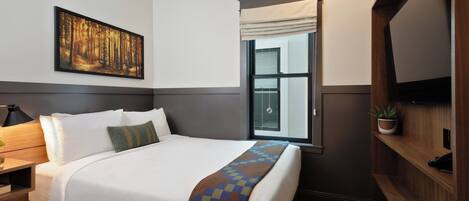 Une chambre d’hôtel avec un grand lit, une table de chevet, une lampe, un tableau, une fenêtre avec des rideaux, un téléviseur et une plante en pot.