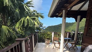 A covered outdoor seating area with two lounge chairs, a potted plant, and a view of a lush green landscape.