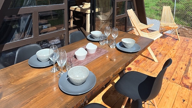 Een eetruimte met een houten tafel gedekt voor vier personen, grote ramen en uitzicht op het landschap.