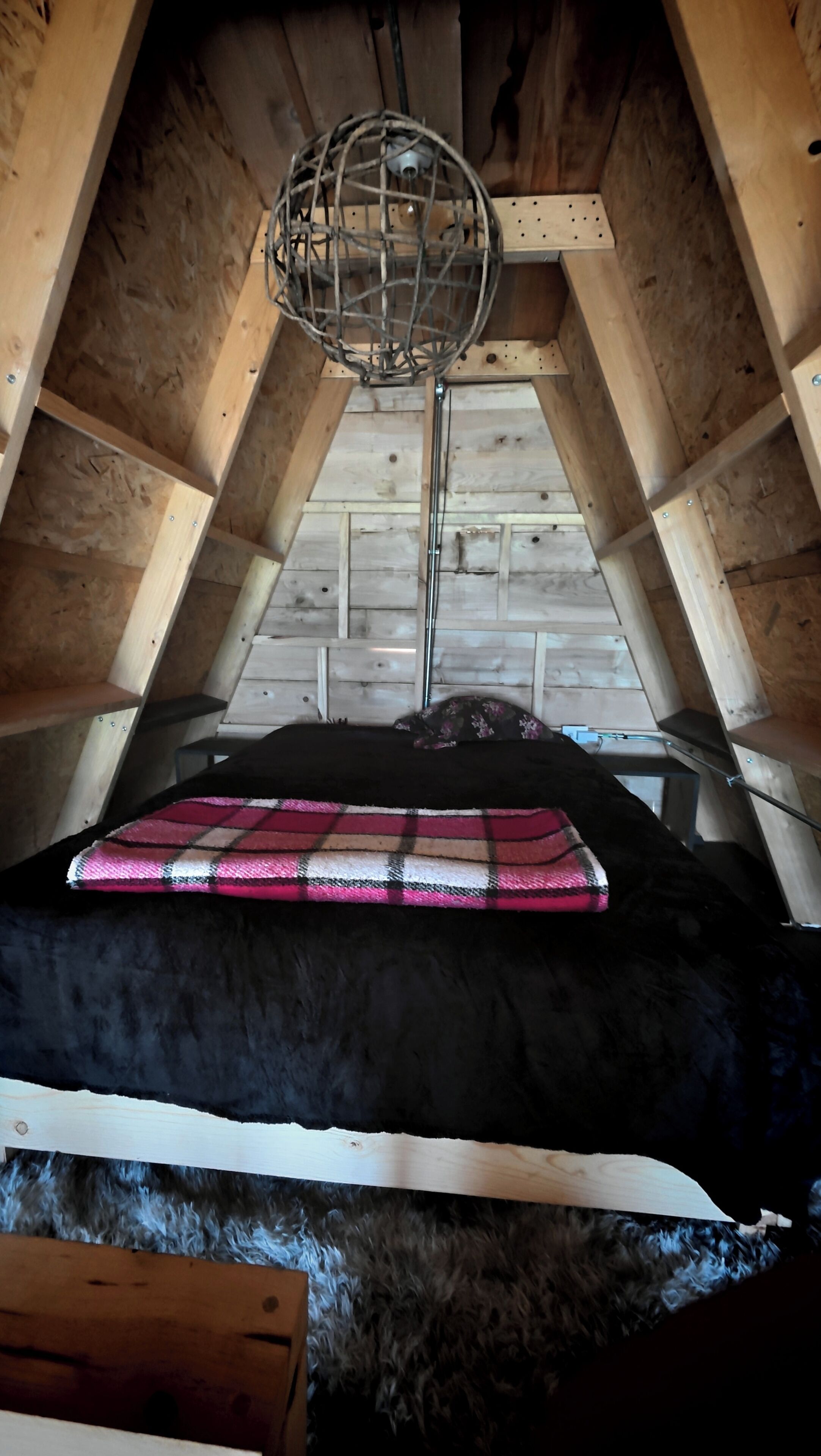 A loft-style bedroom with a sloped ceiling, a metal light fixture, and a plaid blanket on the bed.