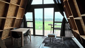 A cozy attic room with a large window, a wooden table, chairs, and a stove.