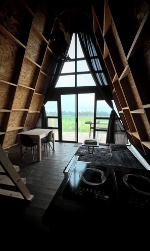 Ein gemütliches Dachzimmer mit einem großen Fenster, einem Holztisch, Stühlen und einem Herd.