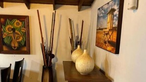 A dining area with a wooden table, chairs, a vase with sticks, and two paintings on the wall.