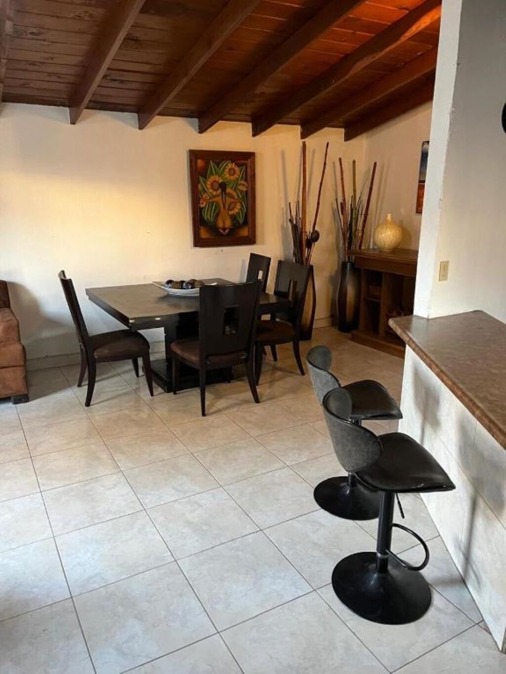 Un coin repas avec une table et des chaises en bois, un tableau au mur et un vase décoré de branches.