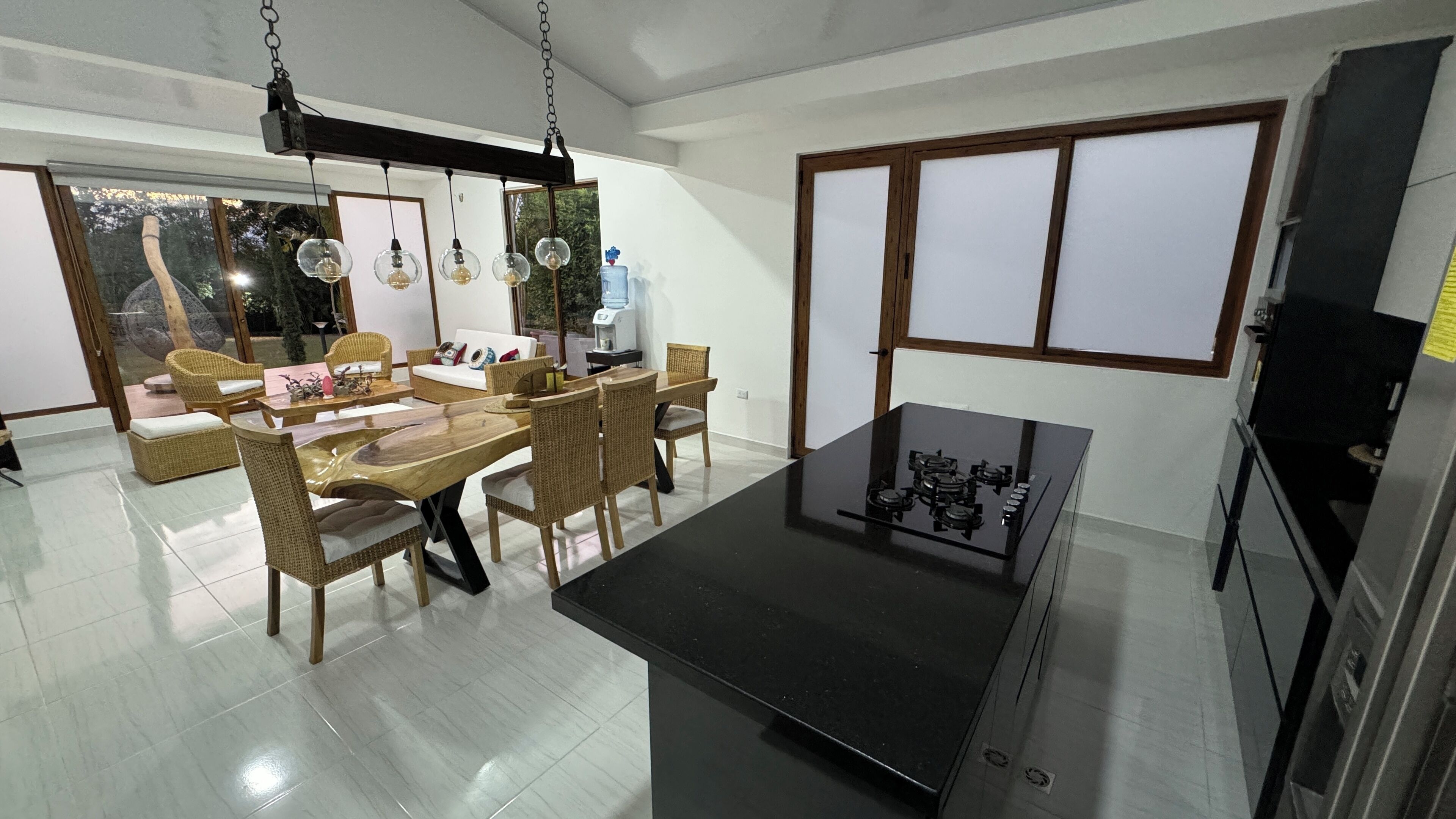 A modern kitchen with a black countertop, a gas stove, and a dining area with wicker furniture.