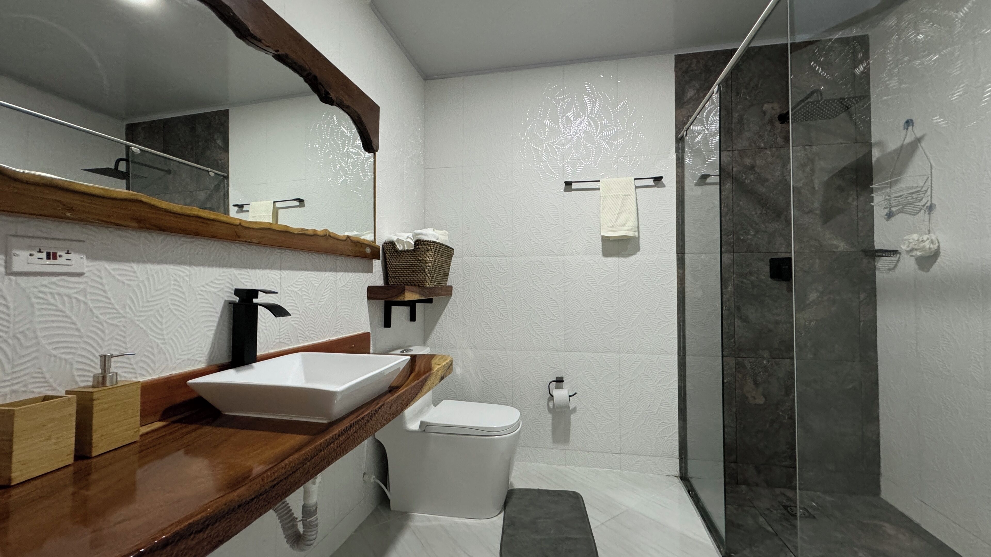 Un bagno moderno con uno specchio grande, un mobile bagno in legno, un lavandino bianco, il water e una cabina doccia in vetro.