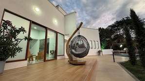 Een modern gebouw met grote glazen deuren, een hangstoel en een houten terras.