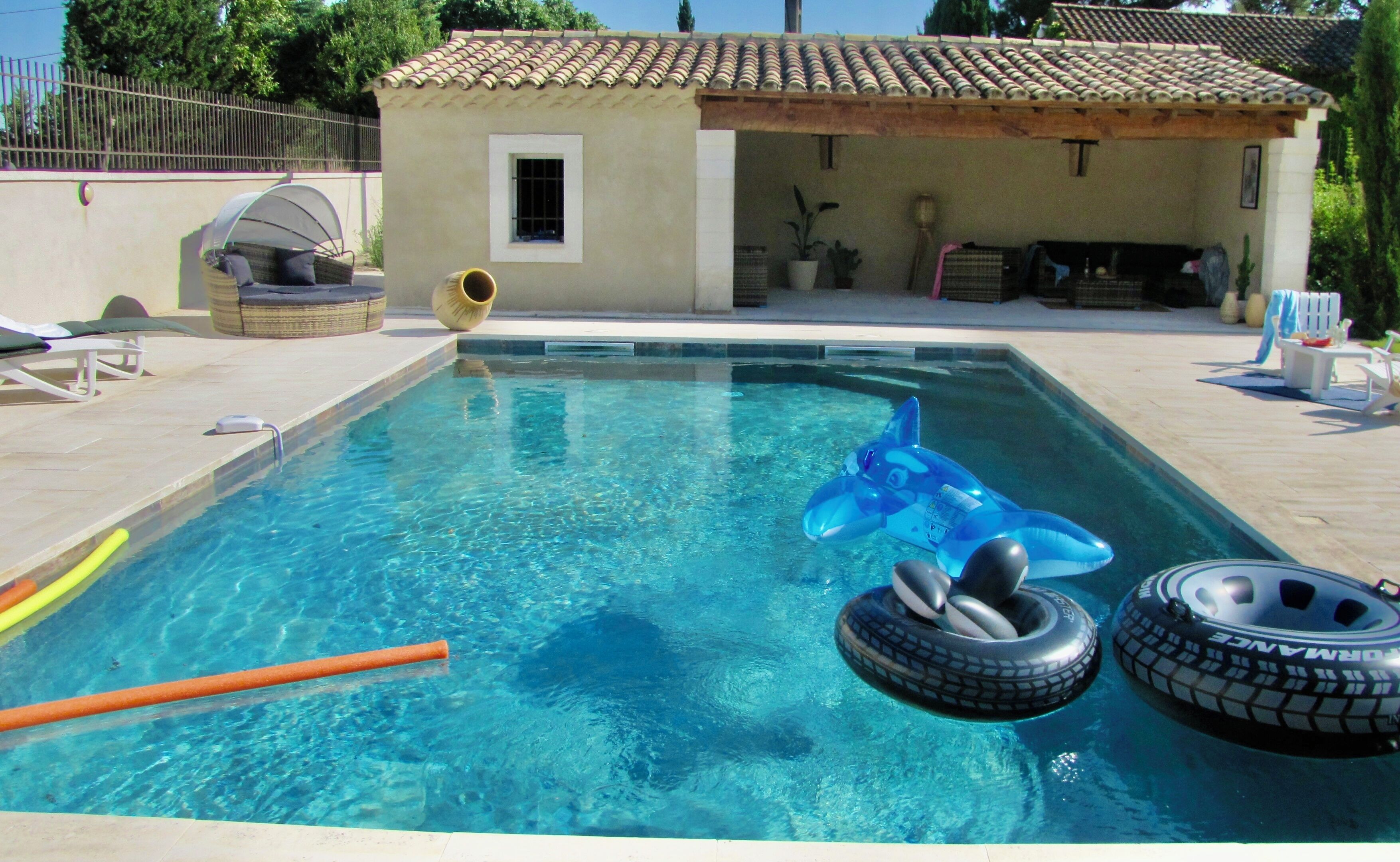 A swimming pool with inflatable toys, a sun lounger, and a small building with a tiled roof.