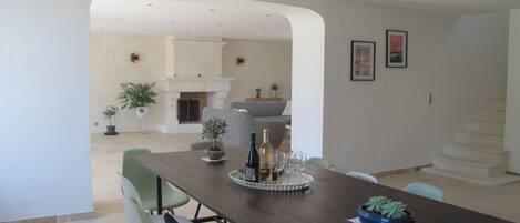 A dining area with a long table, chairs, and a fireplace in the background.