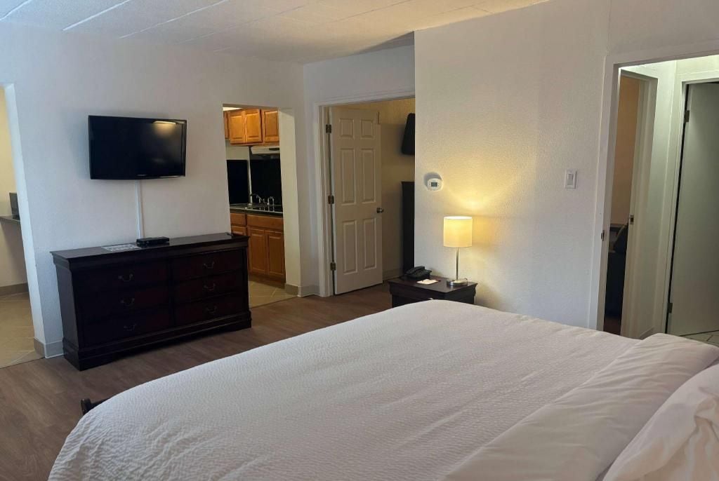 Une chambre d’hôtel comprenant un lit, un téléviseur fixé au mur, une commode et une porte donnant accès à une salle de bain.