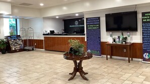 A reception area with a desk, a television, informational posters, and a potted plant. - Tesla Biohealing Wellness Hotel & Resort, Ramada by Wyndham (Butler)