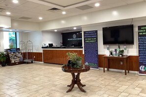 A reception area with a desk, a TV, informational posters, and a potted plant. - Tesla Biohealing Wellness Hotel & Resort, Ramada by Wyndham (Butler)