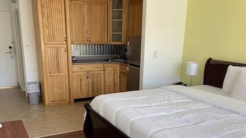 Une chambre d’hôtel comprenant un lit, des armoires en bois, une kitchenette et une poubelle.