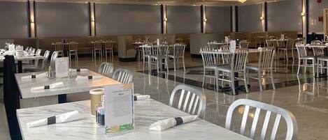 A hotel dining area with marble tables, white chairs, and chandeliers.