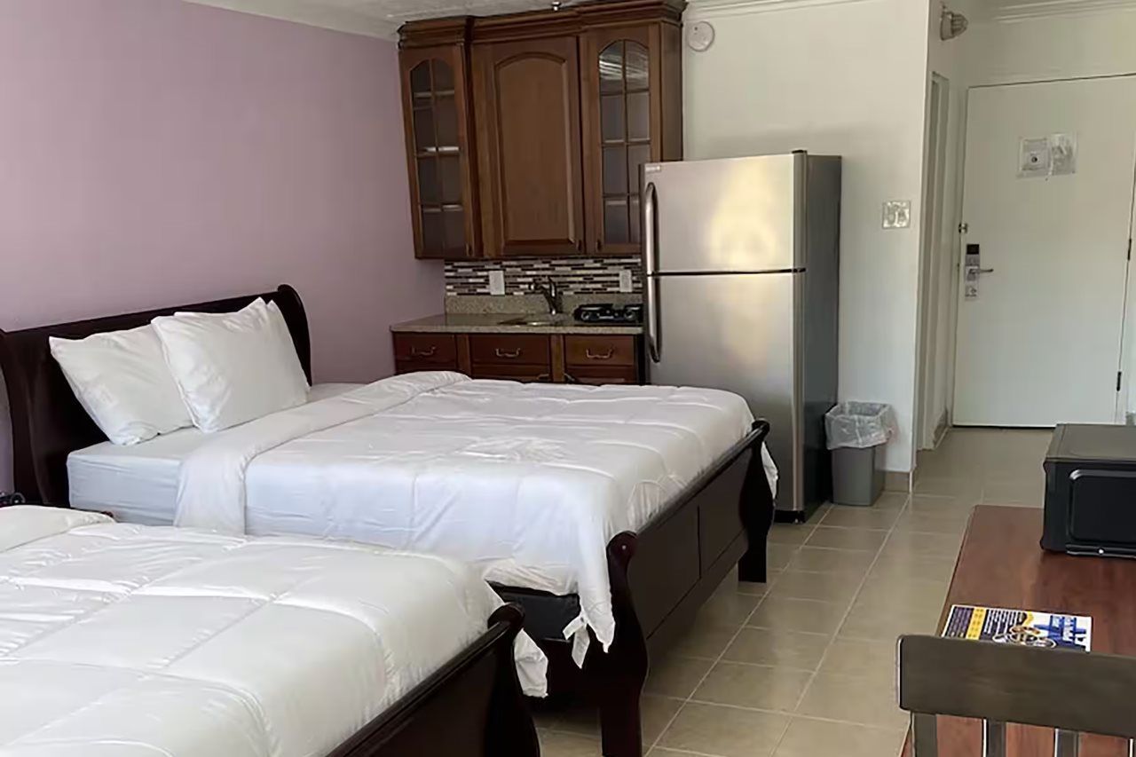 A hotel room with two beds, a kitchenette, a refrigerator, and a trash bin.