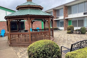 A gazebo with a green roof, a brick building in the background, and a paved patio area. - Tesla Biohealing Wellness Hotel & Resort, Ramada by Wyndham (Butler)