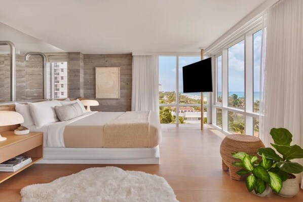 Ein modernes Schlafzimmer mit einem großen Bett, einem Fernseher und Blick auf den Ozean.