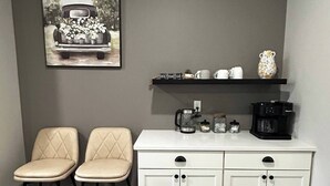 A kitchen with two beige upholstered chairs, a white cabinet with black handles, a coffee maker, and a shelf with mugs and a decorative vase. - Silver Leaf (Stillwater)
