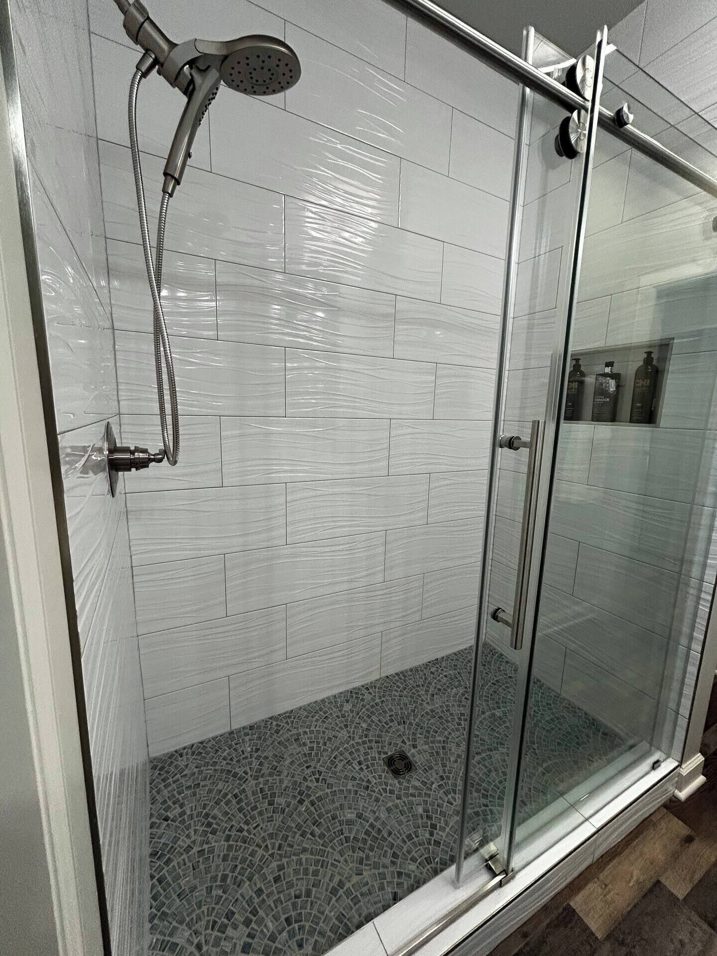 Una ducha con cerramiento de vidrio, suelo de baldosas y ducha.