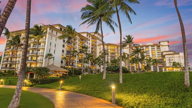 A multi-story hotel with balconies, surrounded by palm trees and a well-maintained lawn.