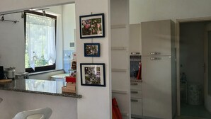 Uma cozinha moderna com bancada branca, um banqueta e uma geladeira.