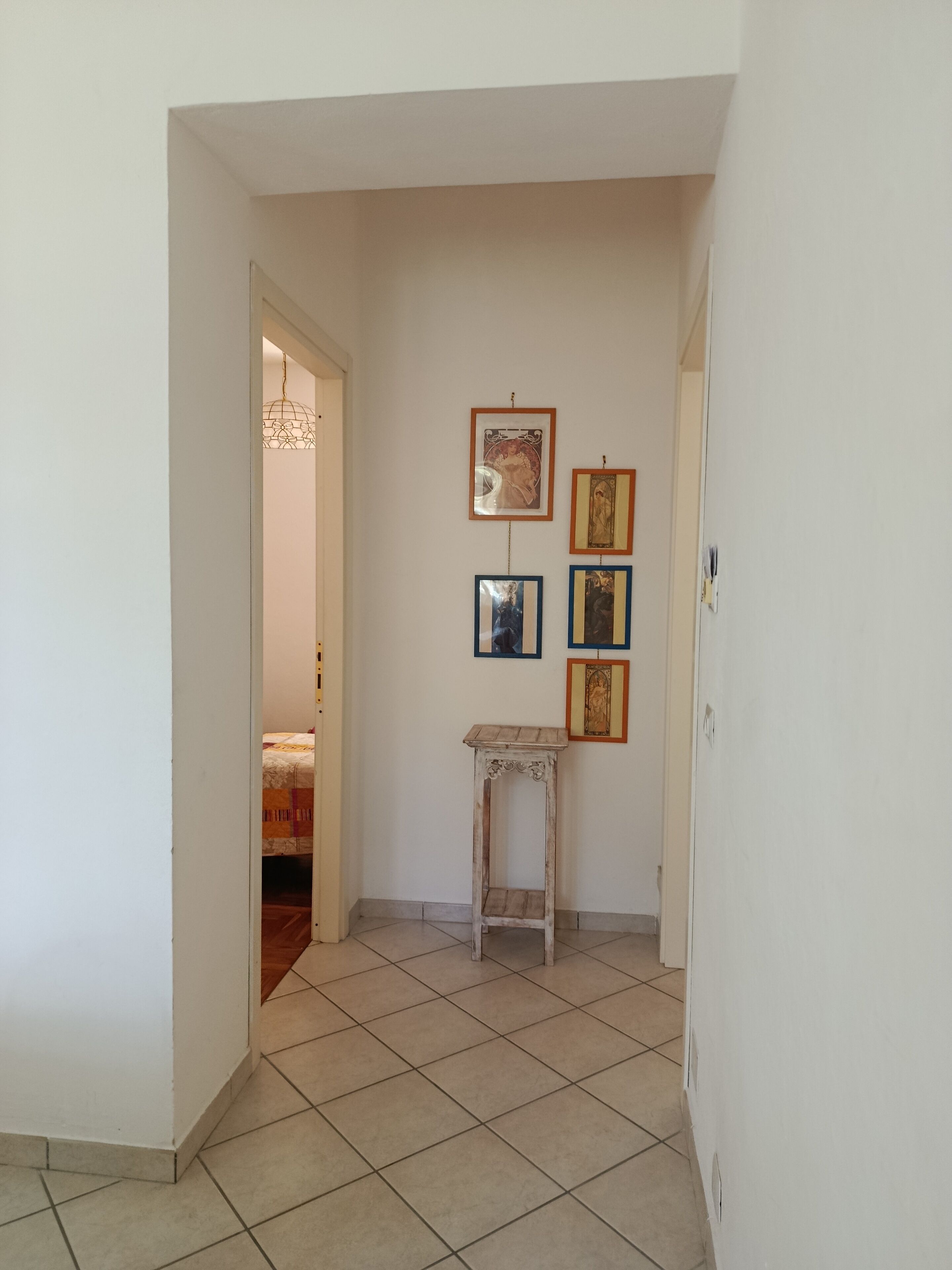 Un pasillo con suelo de baldosas, una mesita de madera y una pared decorada con cuadros.