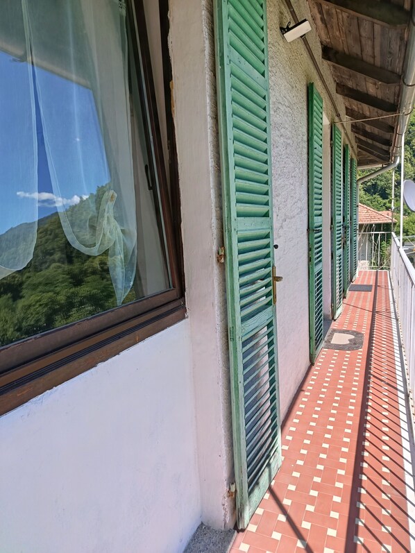 A balcony with green shutters, a tiled floor, and a view of greenery through a window.