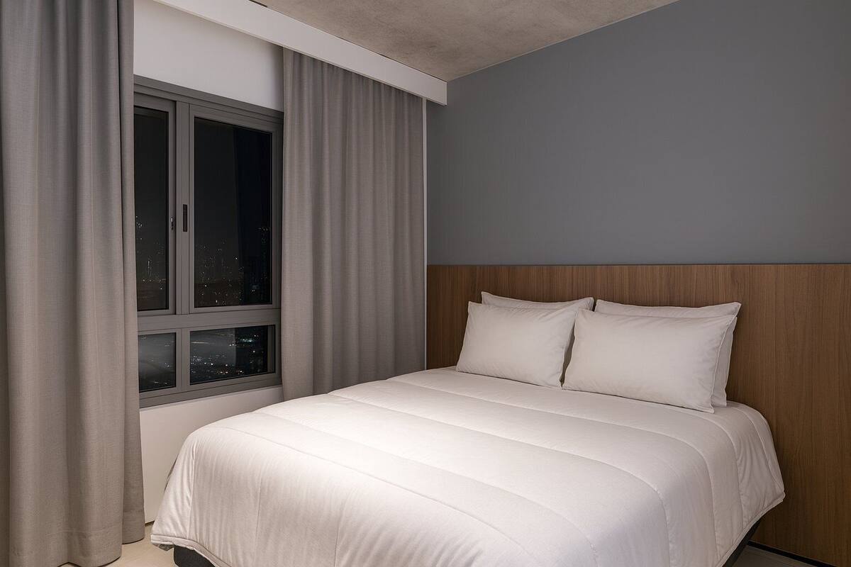 Ein Hotelzimmer mit Bett, Vorhängen und einem Fenster mit Blick auf die Stadt.