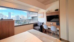 Una habitación de hotel moderna con cama, escritorio, televisor y balcón con vistas a la ciudad.