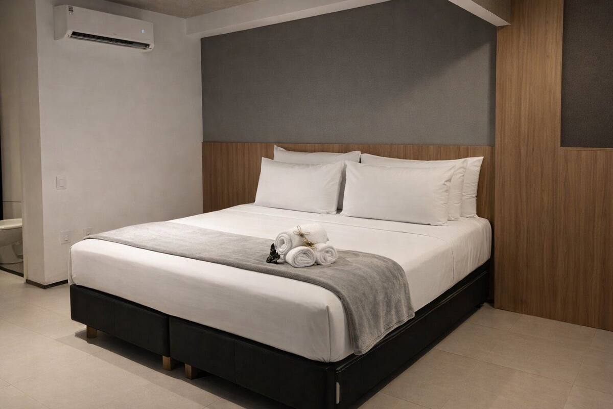 Ein modernes Hotelzimmer mit einem großen Bett, einem Holz-Kopfteil und einer grauen Tagesdecke.