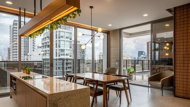 Una cocina moderna con una isla grande, comedor con sillas y ventanas amplias que ofrecen vistas a la ciudad.