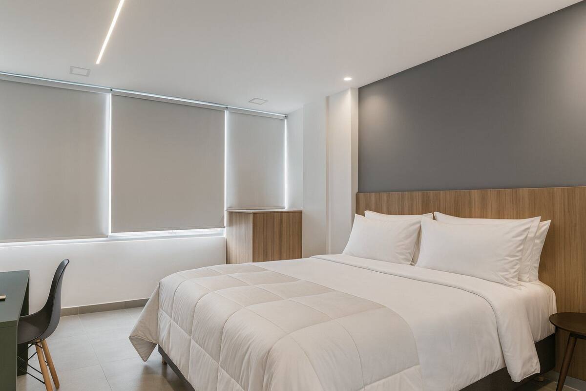 Ein modernes Schlafzimmer mit einem großen Bett, einem Schreibtisch und einem Fenster mit Jalousien.