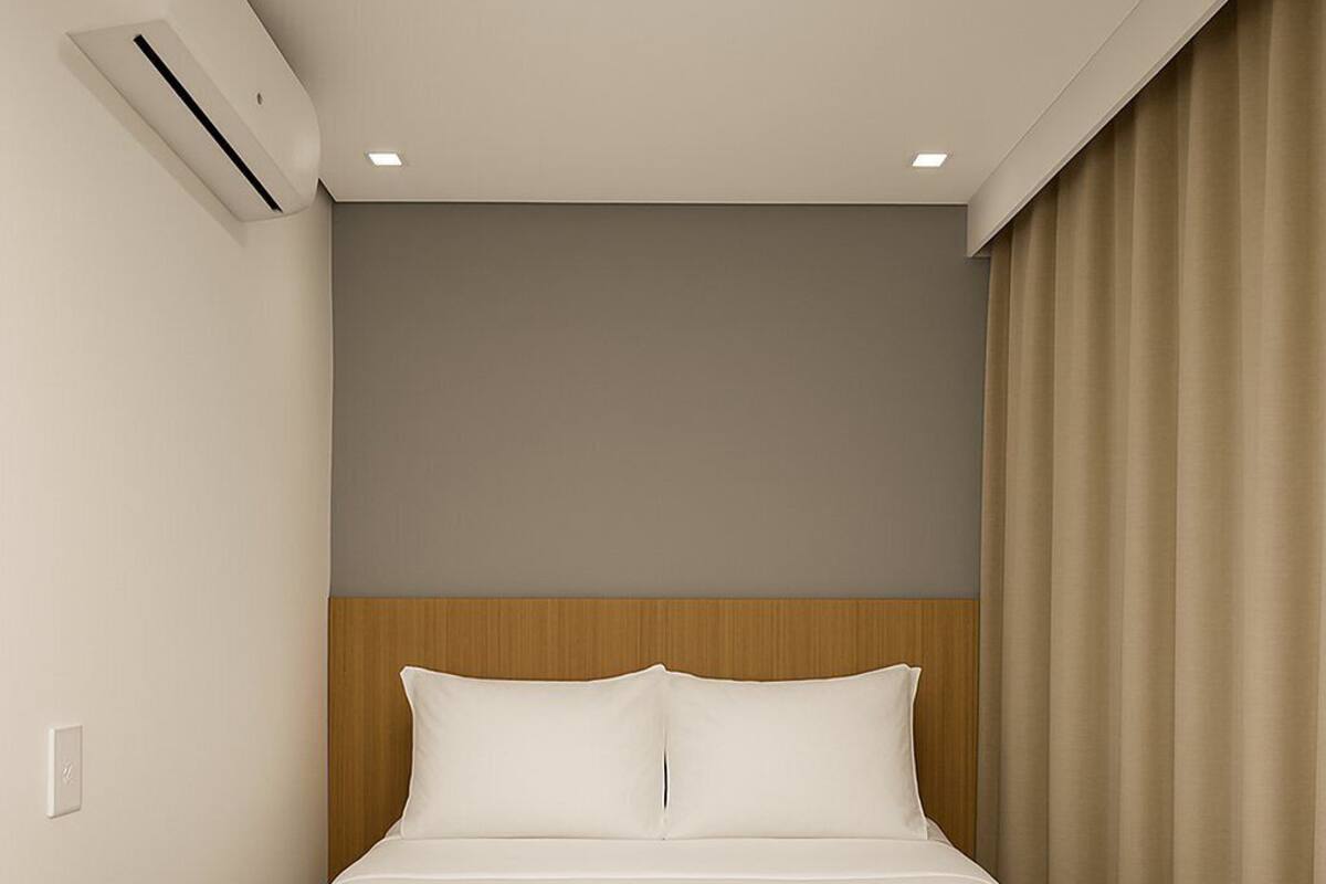 Ein Hotelzimmer mit einem Bett, einem hölzernen Kopfteil, einer grauen Decke und beigen Vorhängen.