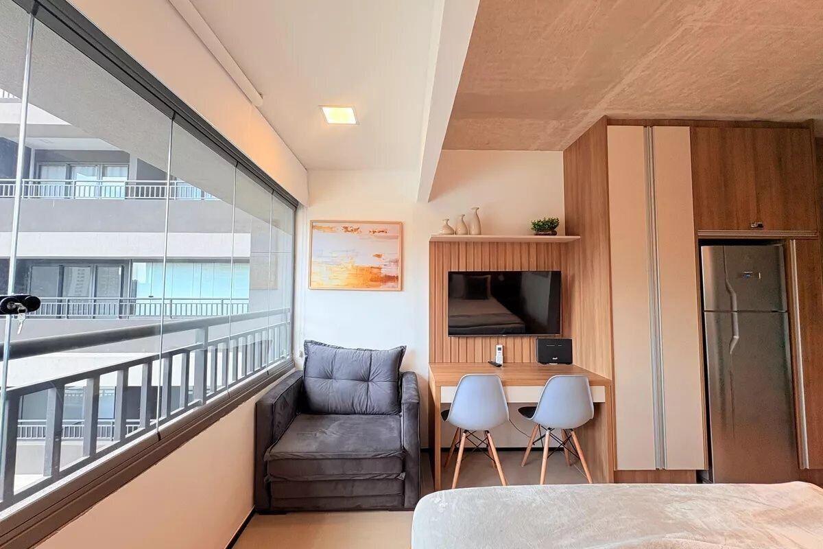 Una habitación de hotel moderna con balcón, sofá, escritorio con dos sillas, televisión y refrigerador.