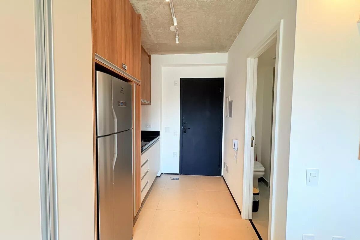 Un pasillo estrecho con un refrigerador de acero inoxidable, una puerta oscura y una pared blanca.