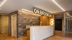 Una recepción con un letrero que dice 'ON BROOKLIN', una pared de piedra, paneles de madera y una lámpara moderna.
