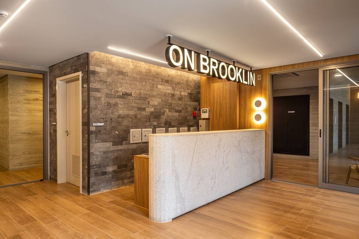 Ein Empfangstresen mit einem Schild, das 'ON BROOKLIN' zeigt, eine Steinwand, Holzvertäfelung und eine moderne Leuchte.