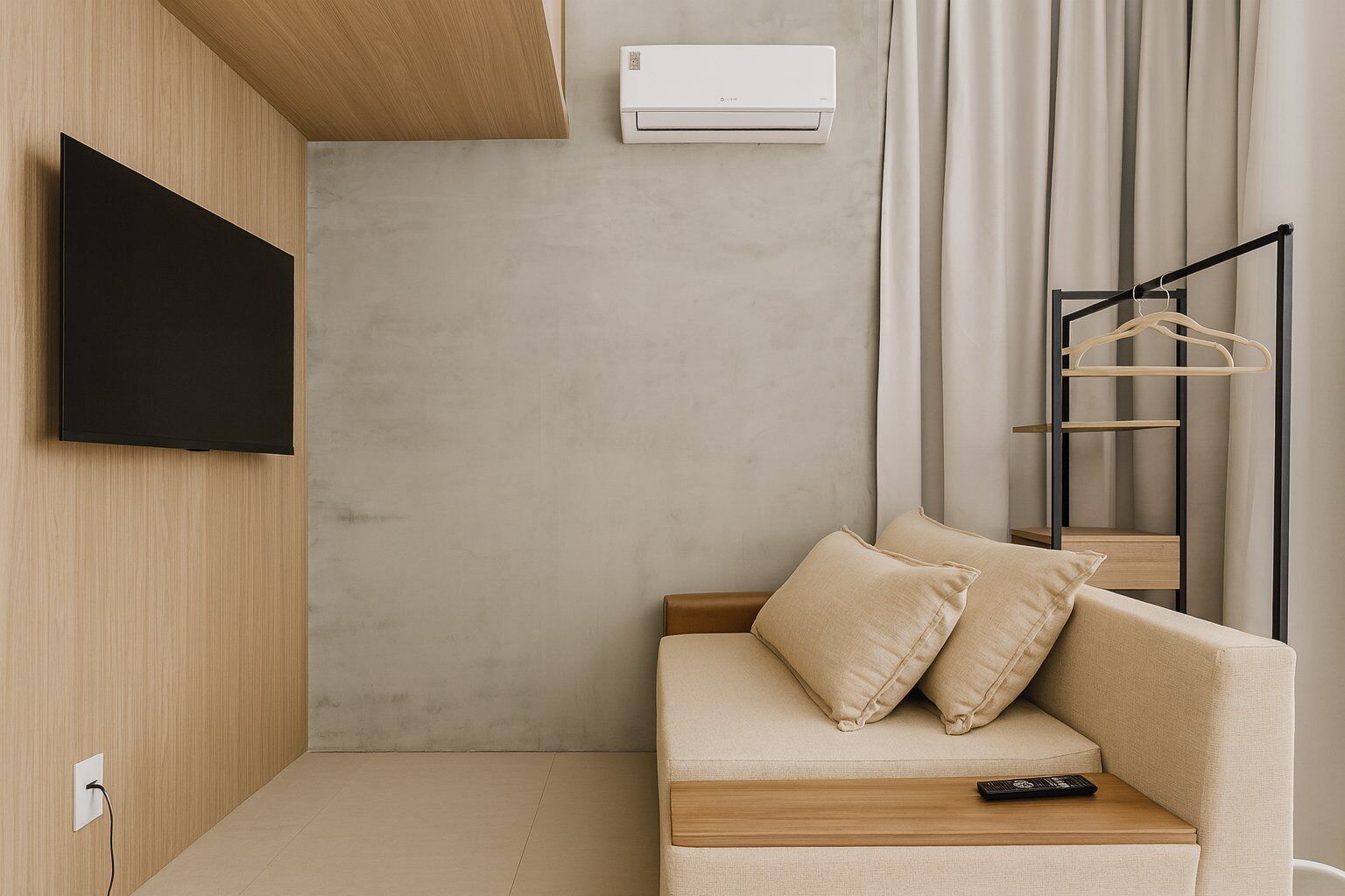 Een moderne kamer met een bank, een aan de muur bevestigde televisie, een airconditioning en een kledingrek.