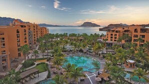 Un resort con varias edificaciones, una piscina central y vista al mar.