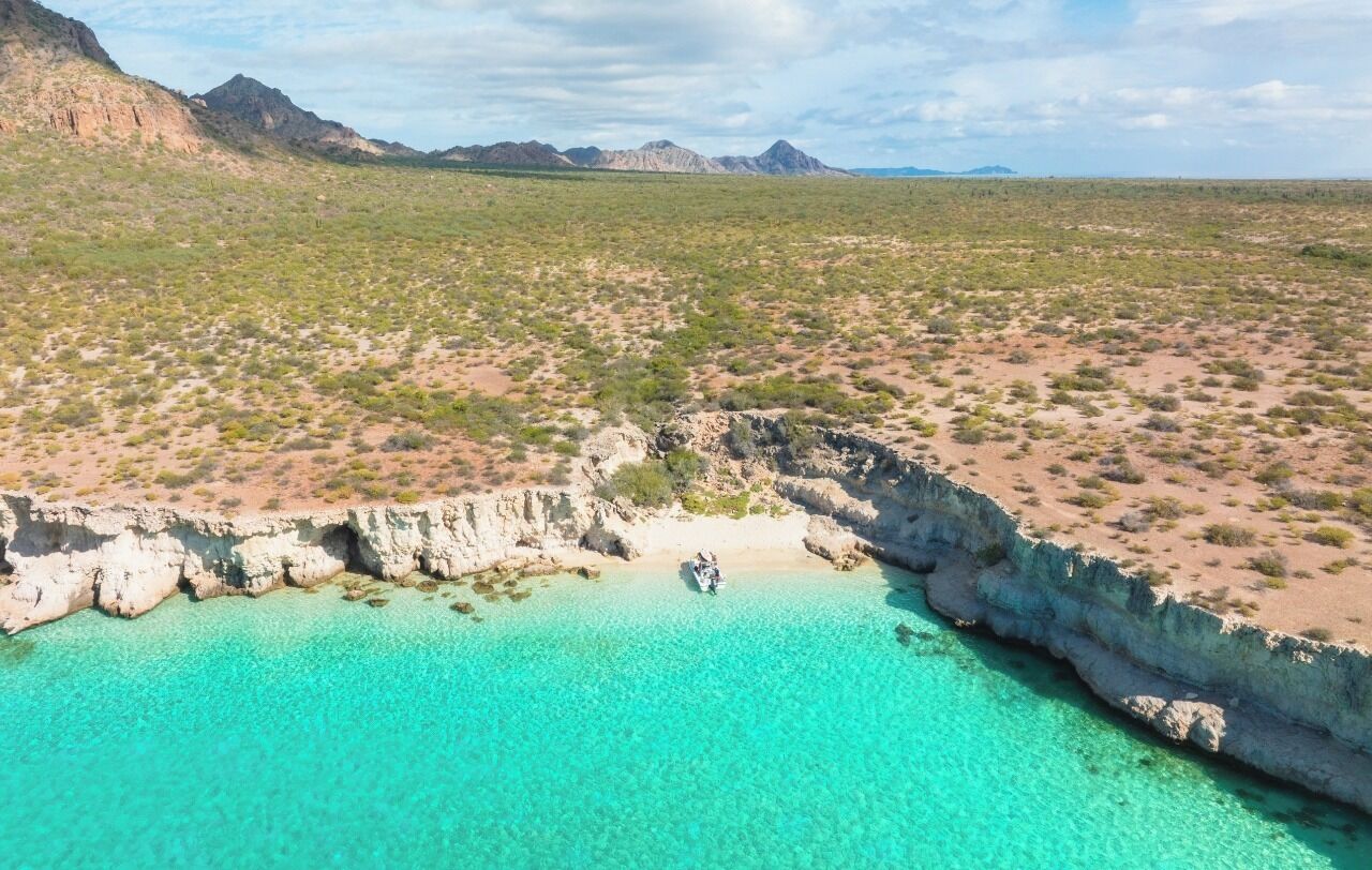A coastal landscape with clear turquoise waters, rocky cliffs, and sparse vegetation.