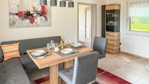 Uma área de refeições com mesa de madeira posta para quatro, cadeiras estofadas cinzas, tapete vermelho e cinza, e uma pintura abstrata moderna na parede.