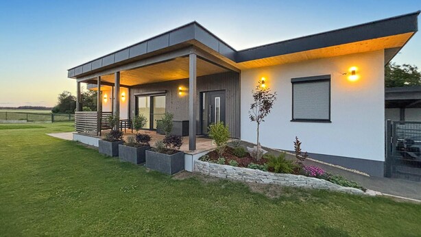 Uma casa moderna com varanda coberta, muro de pedra e gramado bem cuidado.