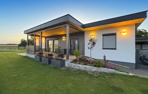 Ein modernes Haus mit überdachter Veranda, einer Steinmauer und einem gepflegten Rasen.