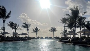 Une piscine à l’eau d’un bleu cristallin, entourée de palmiers et de chaises longues placées sous des parasols.