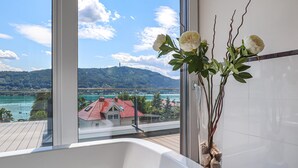 A bathroom with a bathtub, a vase with flowers, and a view of a lake and buildings.