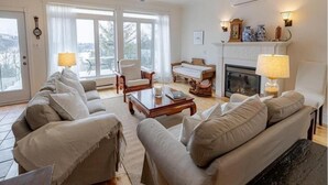 Ein geräumiges Wohnzimmer mit Kamin, Deckenventilator und großen Fenstern.